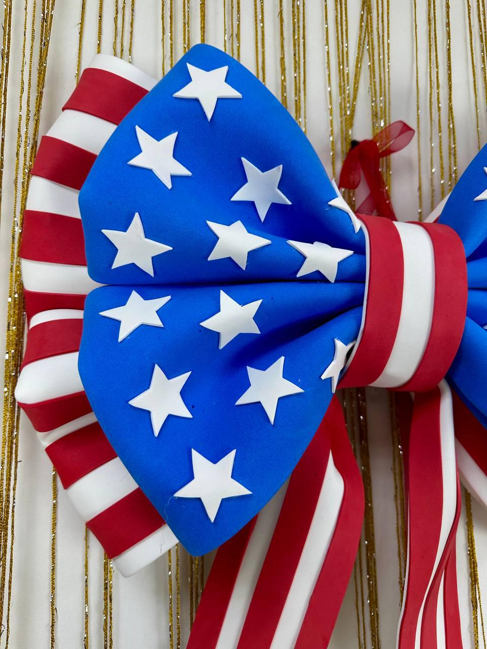 May include: A patriotic bow featuring a blue center with white stars and red and white striped accents. The bow is a festive decoration, perfect for Independence Day or other patriotic events. The bow is made of a sturdy material.