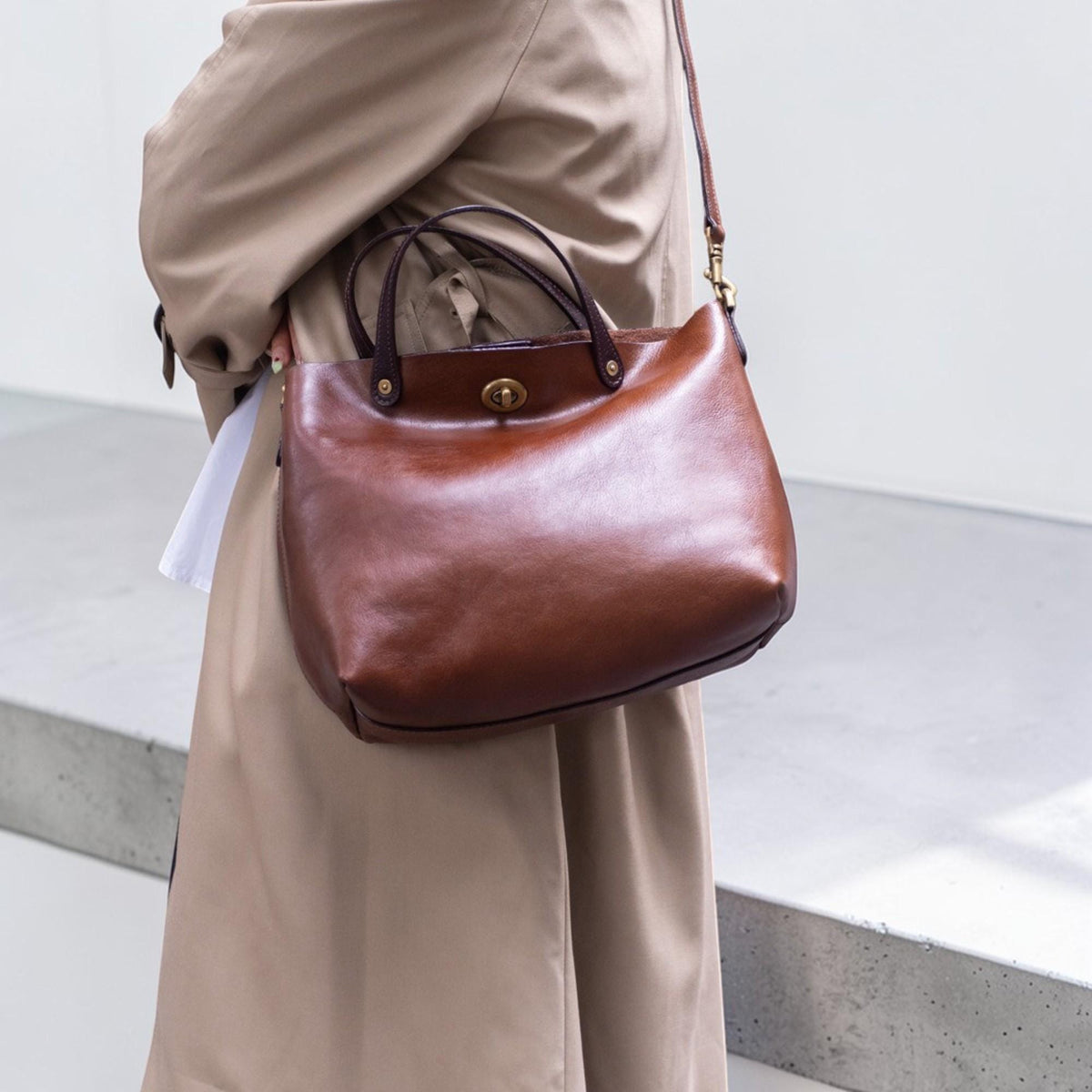 May include: A brown leather tote bag with a top handle and a detachable shoulder strap. The bag has a classic design with a gold-colored clasp and dark brown accents. The bag is made of smooth, polished leather.
