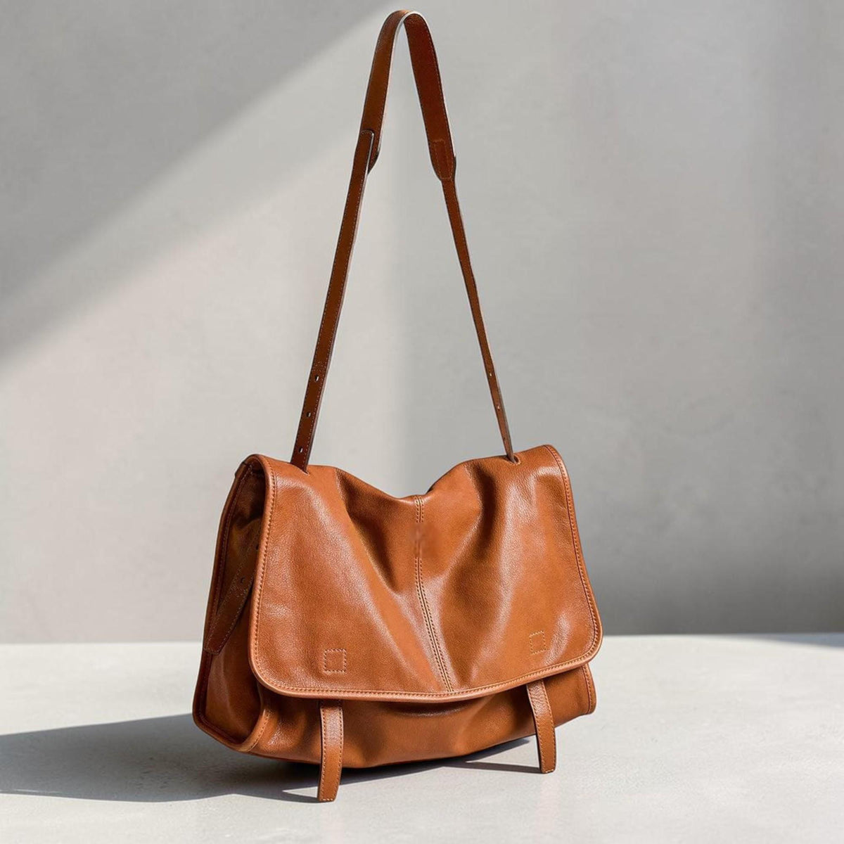 May include: A brown leather messenger bag with a long adjustable shoulder strap. The bag has a flap closure and two buckle straps on the front. The leather has a slightly wrinkled texture. The bag is designed to be worn over the shoulder.