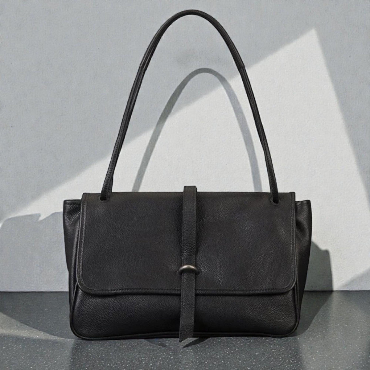 May include: Black leather shoulder bag with a flap closure and a long strap. The bag has a rectangular shape with a strap that secures the flap. The bag is made of a smooth, matte leather.