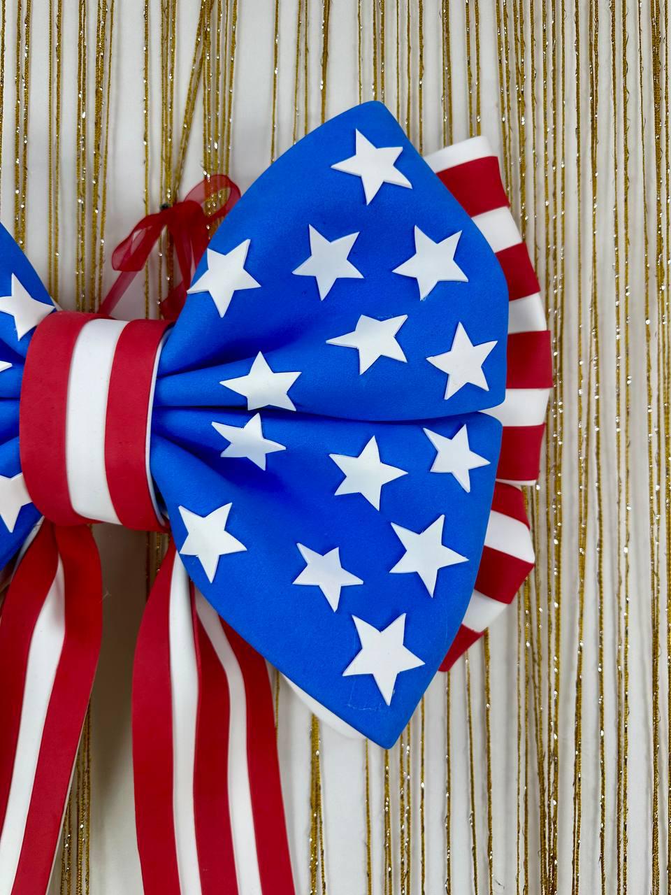 May include: A large patriotic bow featuring a blue section with white stars and red and white striped sections. The bow is tied with a red ribbon and is likely for decoration.