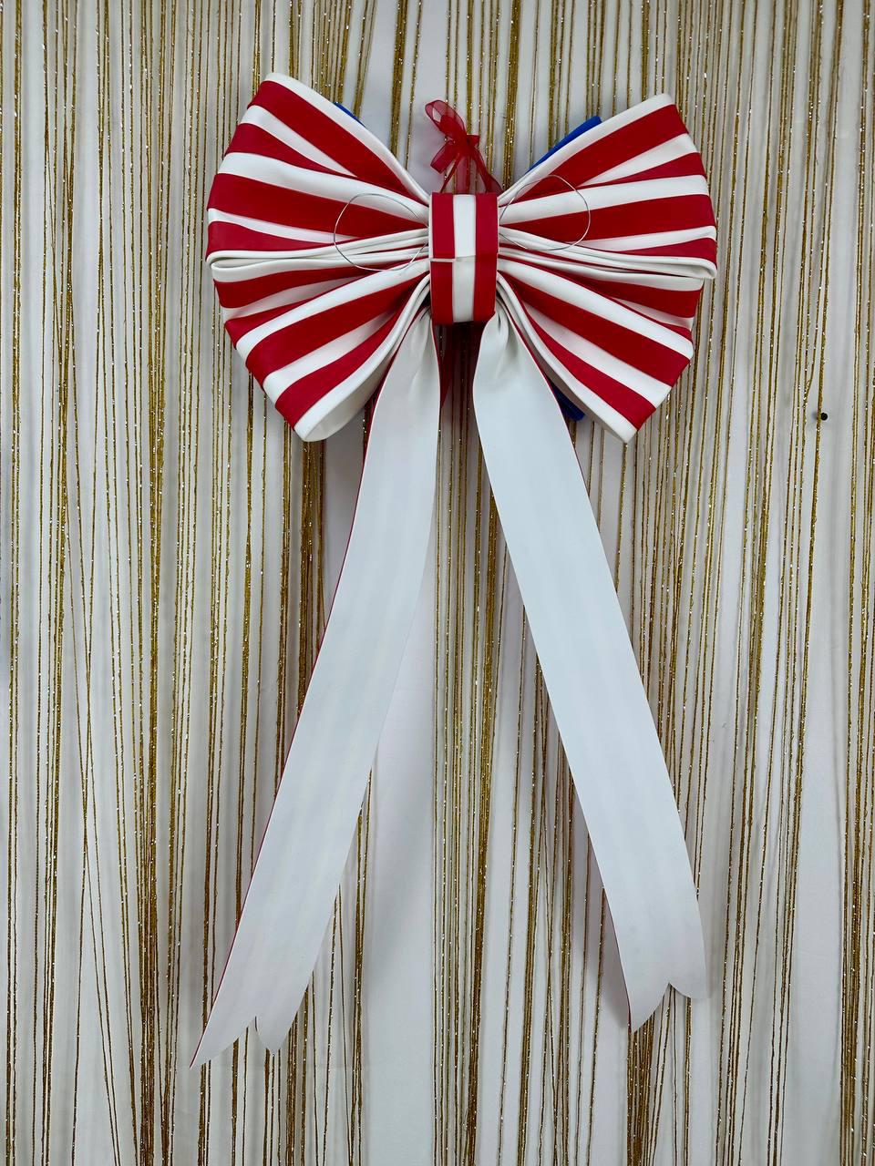 May include: A large decorative bow with red and white striped fabric, featuring long white streamers. The bow is accented with a small red ribbon and is likely used for festive decorations or gift wrapping.