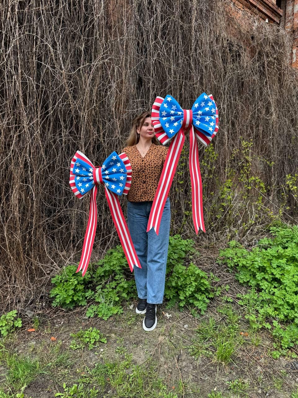May include: Two large decorative bows with a patriotic theme. The bows feature a blue center with white stars and red and white striped ribbons. The bows are designed to be used as decorations for the Fourth of July or other patriotic events.