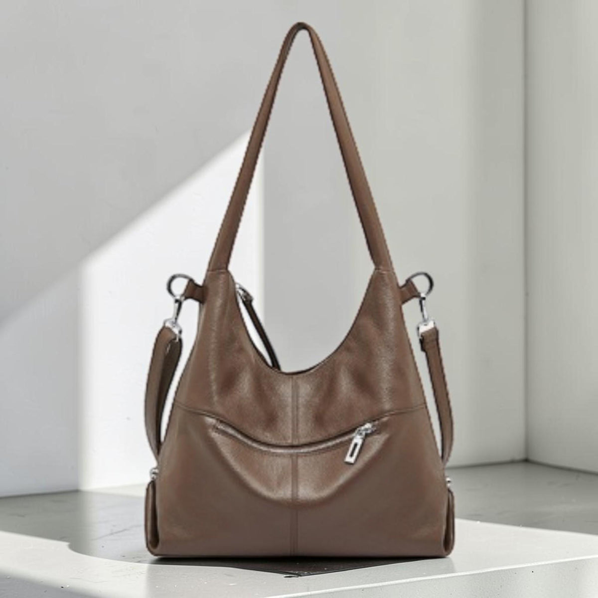 May include: A brown leather shoulder bag with a zipper pocket and adjustable straps. The bag has a curved shape and a long strap for carrying over the shoulder. The bag is made of a soft, supple leather.