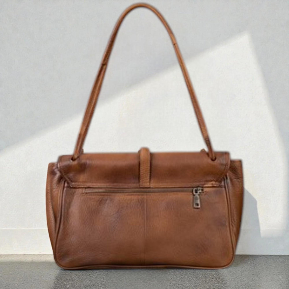 May include: A brown leather shoulder bag with a rectangular shape and a long handle. The bag has a flap closure with a buckle and a zipper pocket on the back. The leather has a textured appearance.