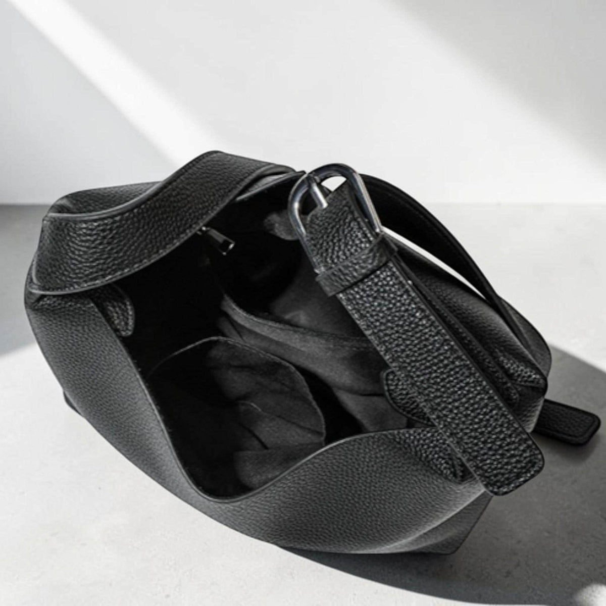 May include: Black leather handbag with a textured finish. The bag has a curved shape with a single strap and a silver-tone metal buckle. The interior of the bag is visible, revealing a dark lining and pockets.