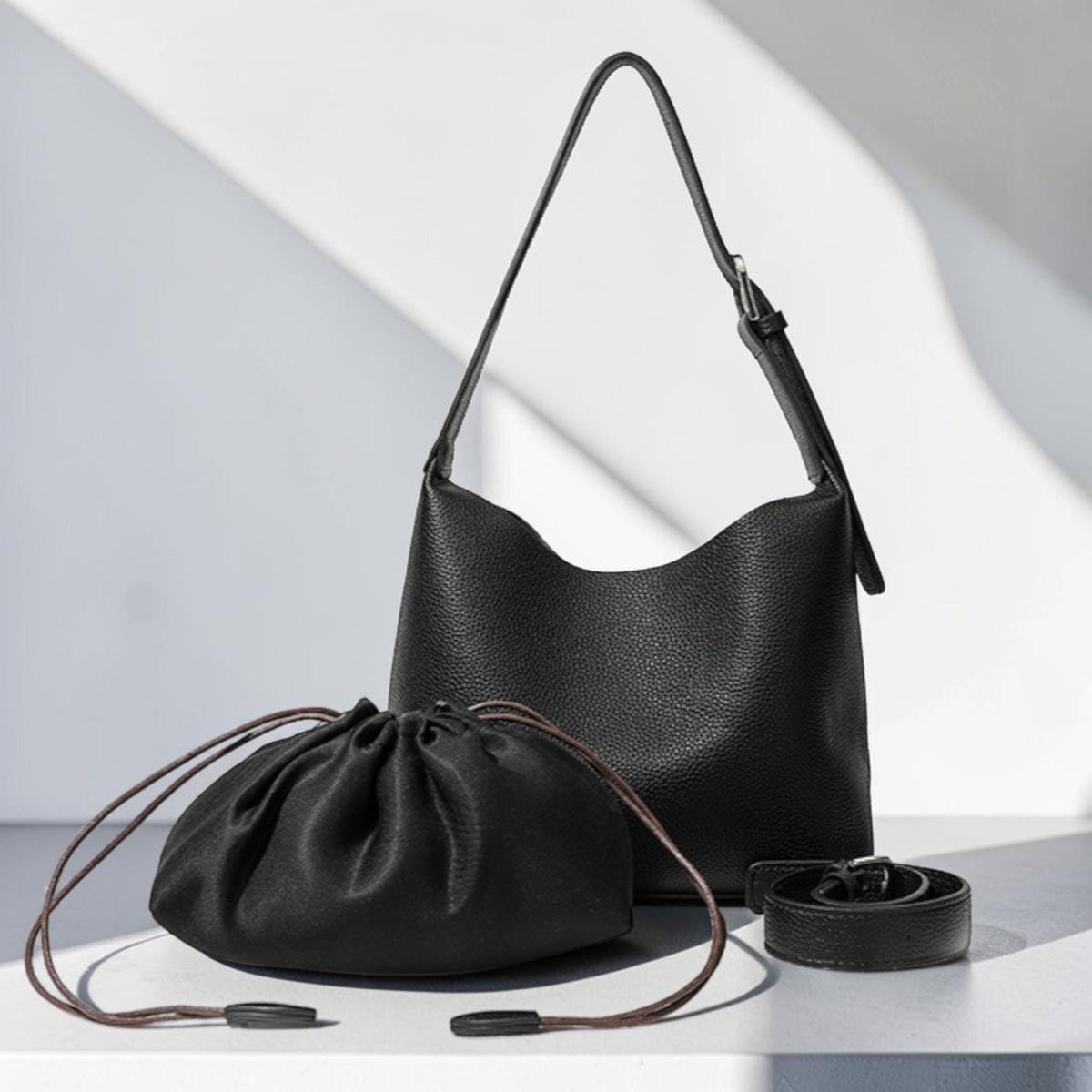 May include: A black leather handbag with a shoulder strap, a drawstring pouch, and a belt. The handbag has a curved top and a textured surface. The drawstring pouch has brown drawstrings. The belt has a silver buckle.