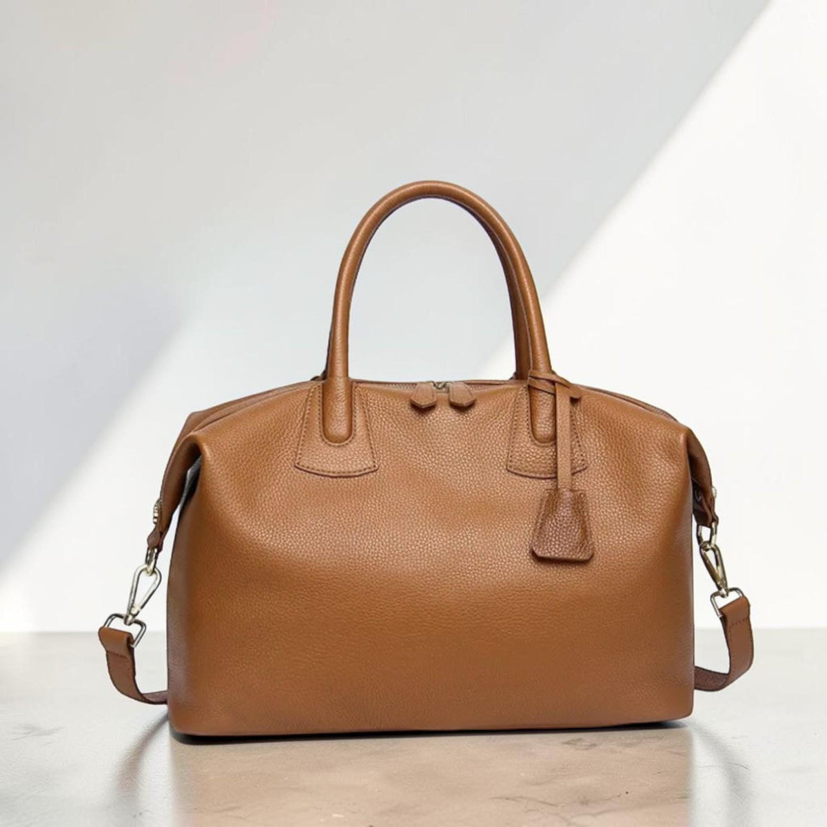 May include: A brown leather satchel bag with a top handle and a detachable shoulder strap. The bag has a zipper closure and a small leather tag attached to the handle. The bag is approximately 12 inches long, 8 inches high, and 6 inches wide.