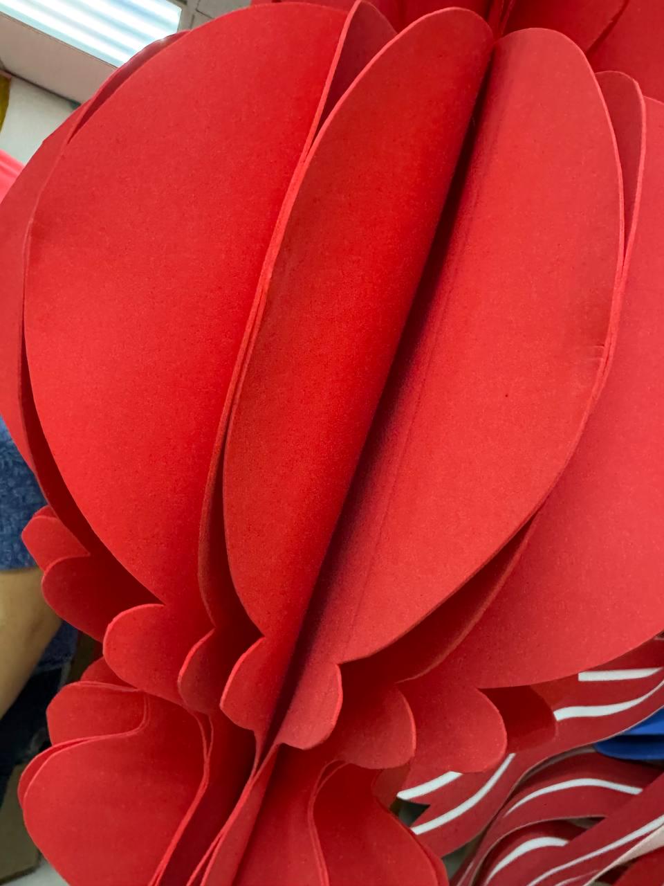 May include: A close-up of a large, vibrant red paper lantern. The lantern is constructed from layered, petal-shaped pieces, creating a three-dimensional effect. The design suggests a festive or decorative item, possibly for celebrations.