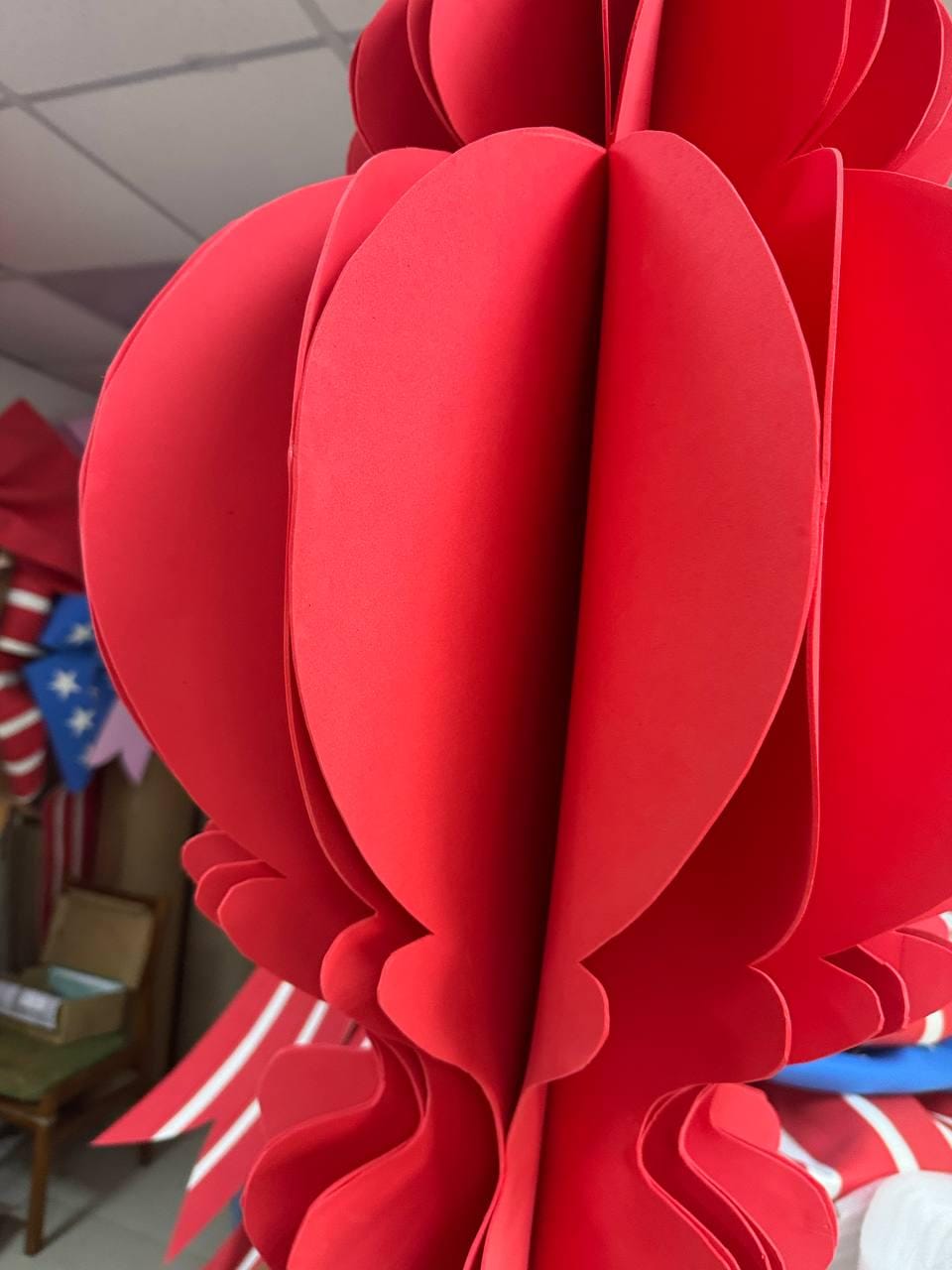 May include: A large, vibrant red paper lantern with a layered, petal-like design. The lantern's form is spherical, with multiple sections creating a three-dimensional effect. The paper is a solid, bright red, and the lantern is likely for decorative purposes.