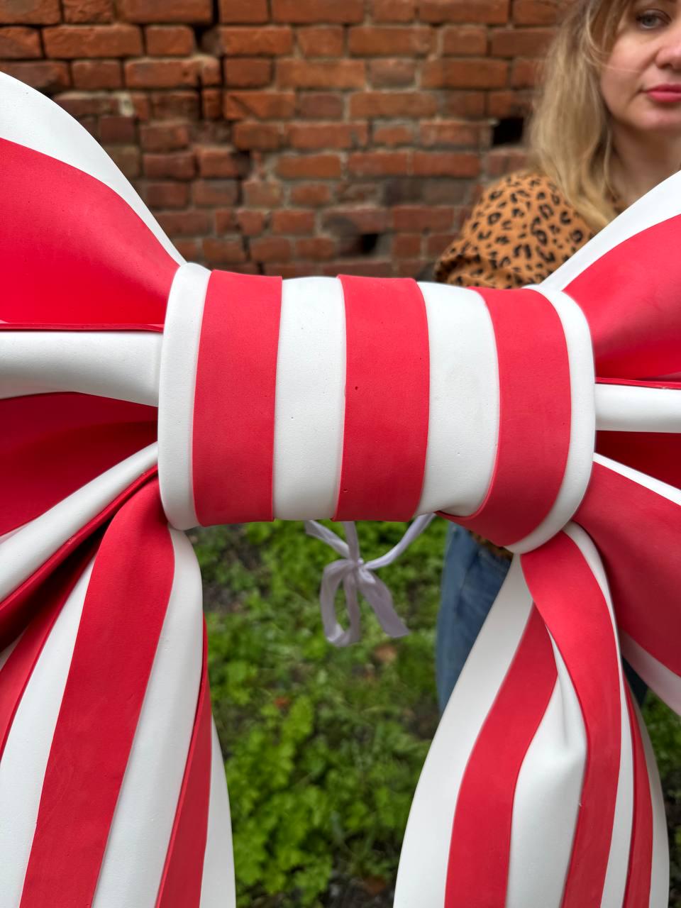 May include: A large, decorative bow with red and white stripes. The bow is made of a glossy material and has a central band with vertical red and white stripes. The bow is tied with a white ribbon.