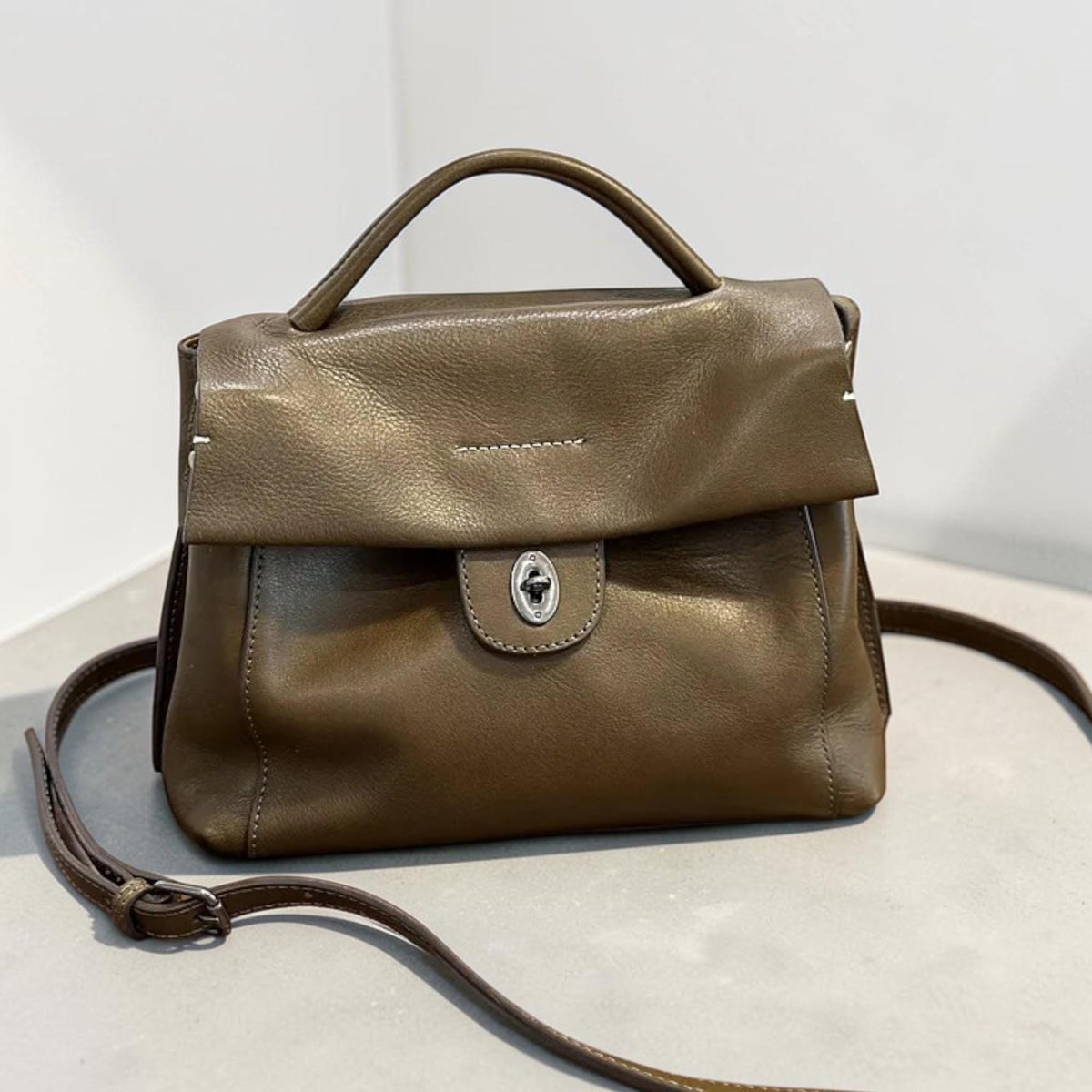 May include: A brown leather handbag with a top handle and a detachable shoulder strap. The bag features a flap closure with a silver-toned clasp. The bag's design includes visible stitching and a structured silhouette, suitable for everyday use.