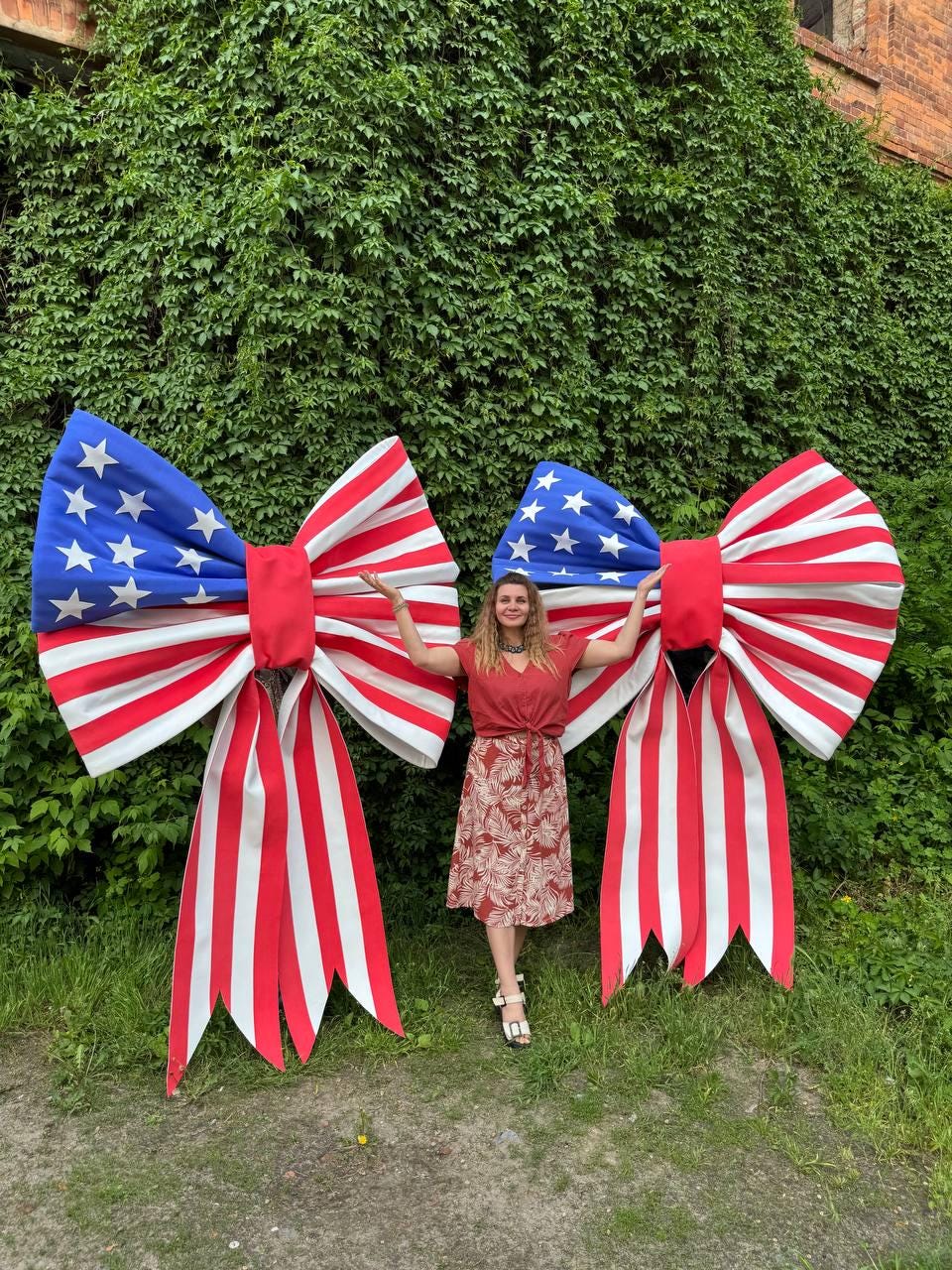 May include: Two large patriotic bows in red, white, and blue, resembling the American flag. The bows have a red center and white and red striped tails. The top section features a blue field with white stars.