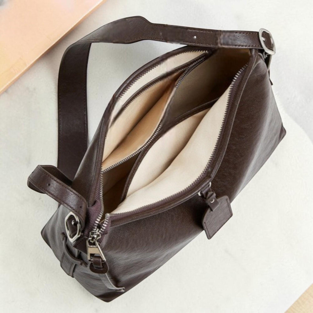 May include: A brown leather shoulder bag with a long adjustable strap. The bag has a rectangular shape with a zipper closure and multiple interior compartments. The interior lining is a light beige color. The bag is shown open, revealing the interior.