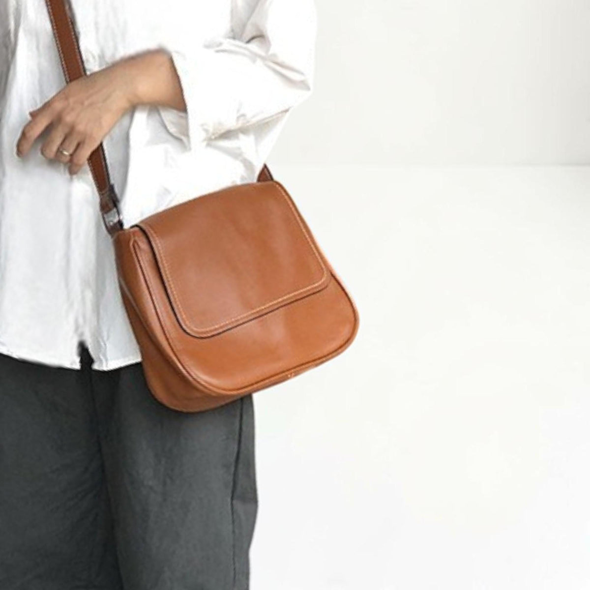 May include: A brown leather crossbody bag with a flap closure. The bag has a rectangular shape with a stitched border and a long, adjustable strap. The bag is a warm, medium brown color.