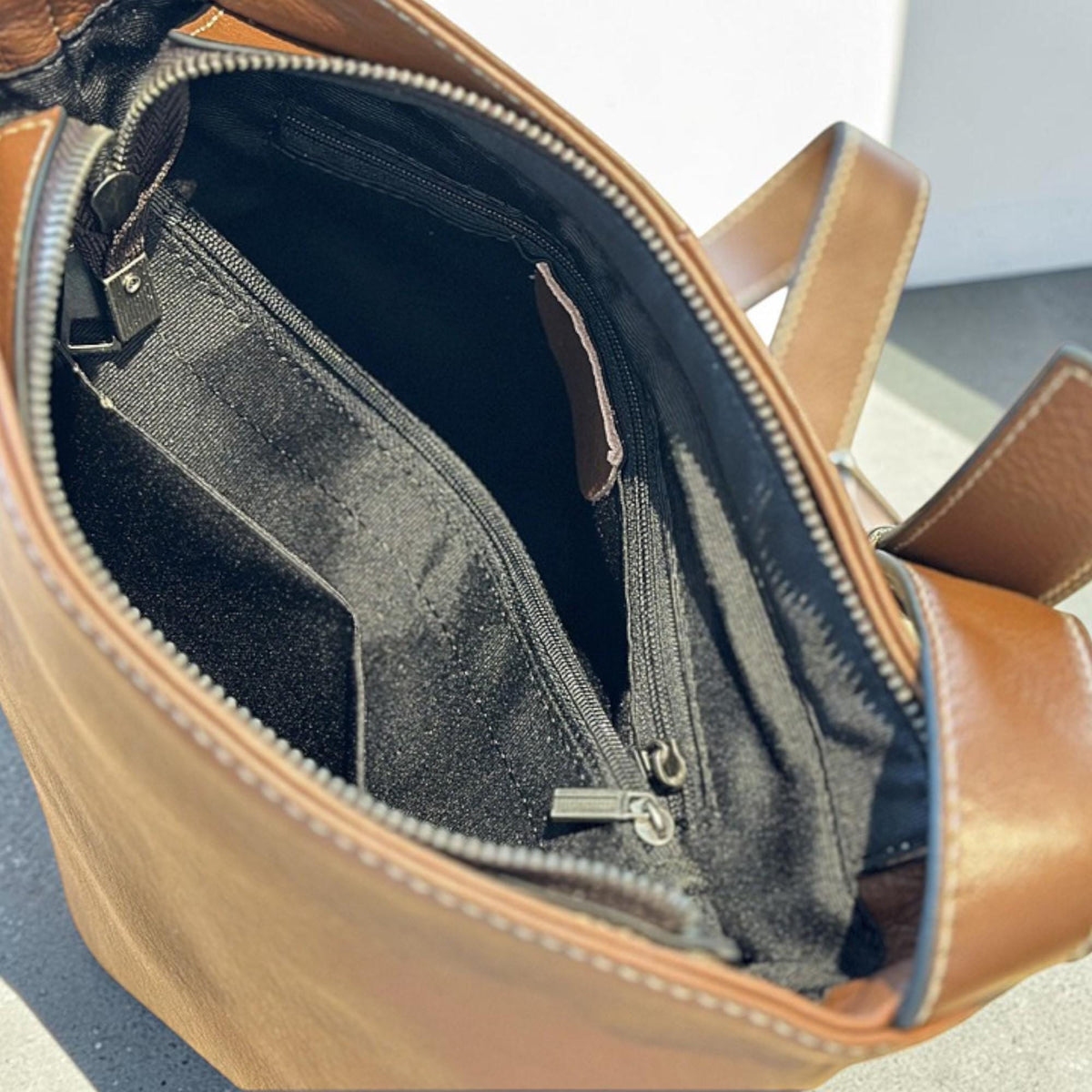 May include: A brown leather shoulder bag with a top zipper and multiple interior compartments. The bag has a dark interior and a contrasting brown strap. The bag is designed with a classic, functional style.