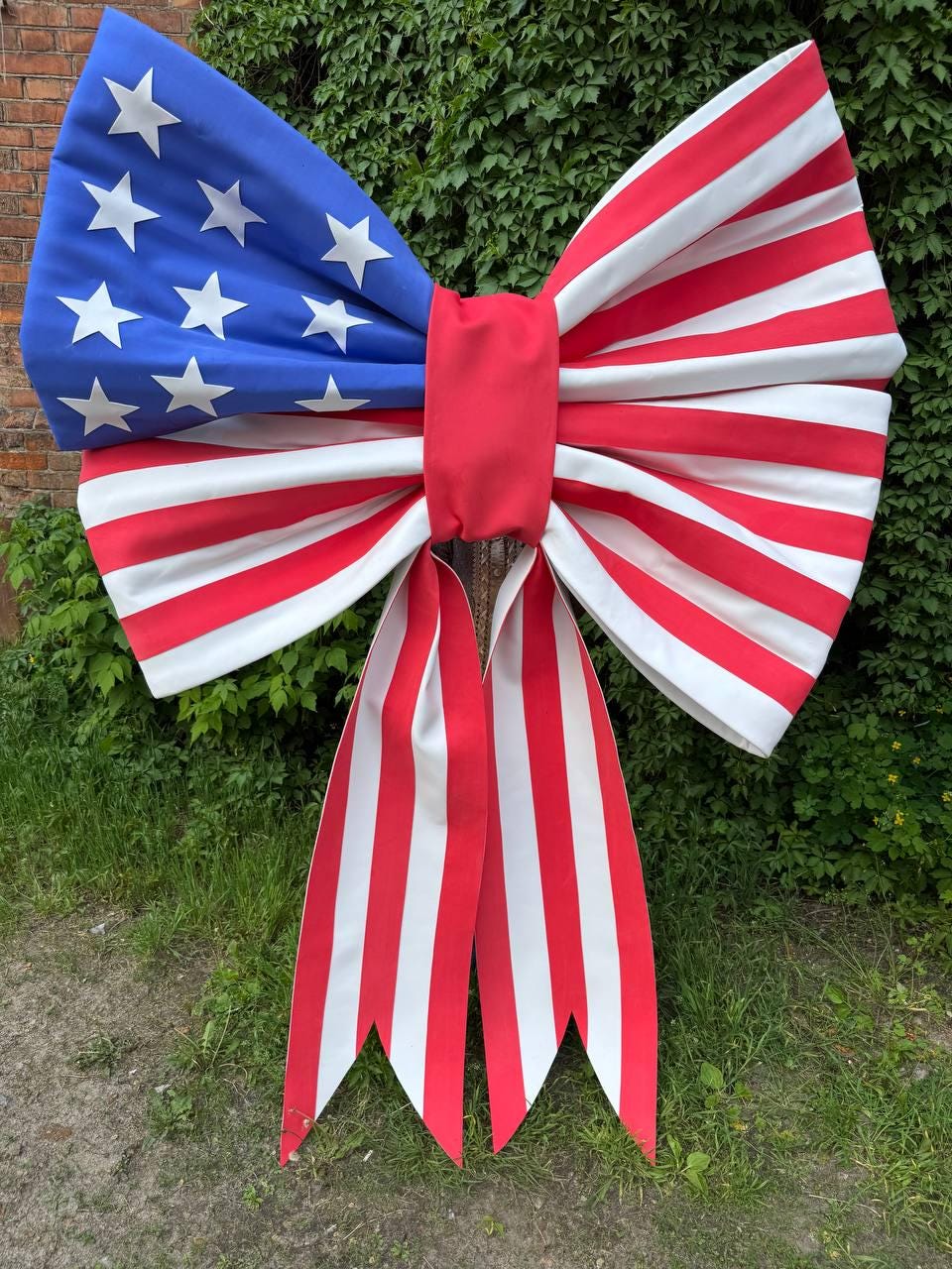 May include: A large decorative bow featuring the American flag design. The bow has a blue section with white stars, and red and white stripes. The bow is made of fabric and has long, striped tails.