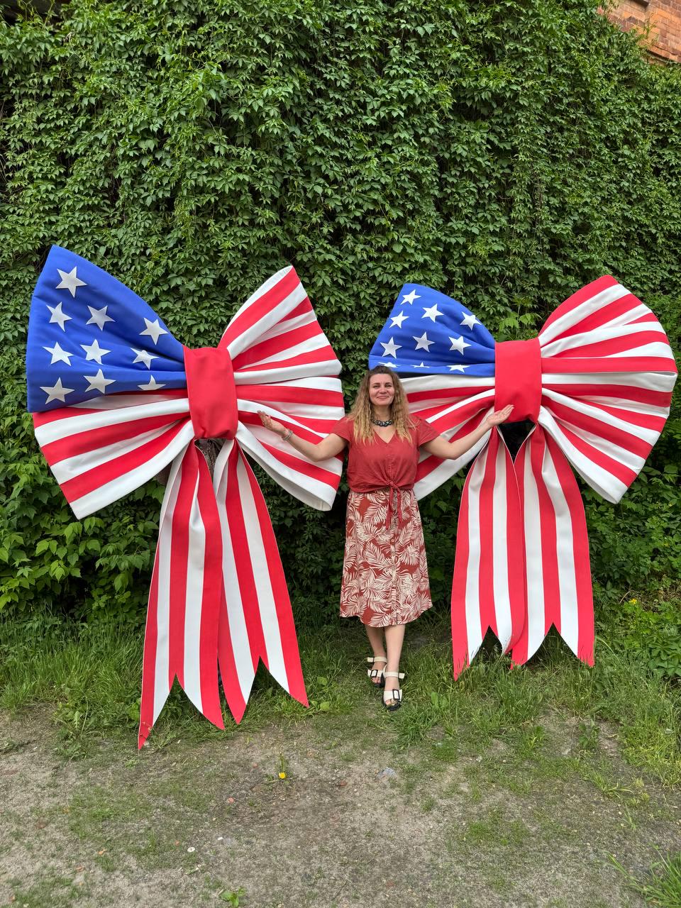 May include: Two large decorative bows with a patriotic design. The bows feature a blue section with white stars and red and white stripes, resembling the American flag. The bows are red in the center and have long, striped tails.