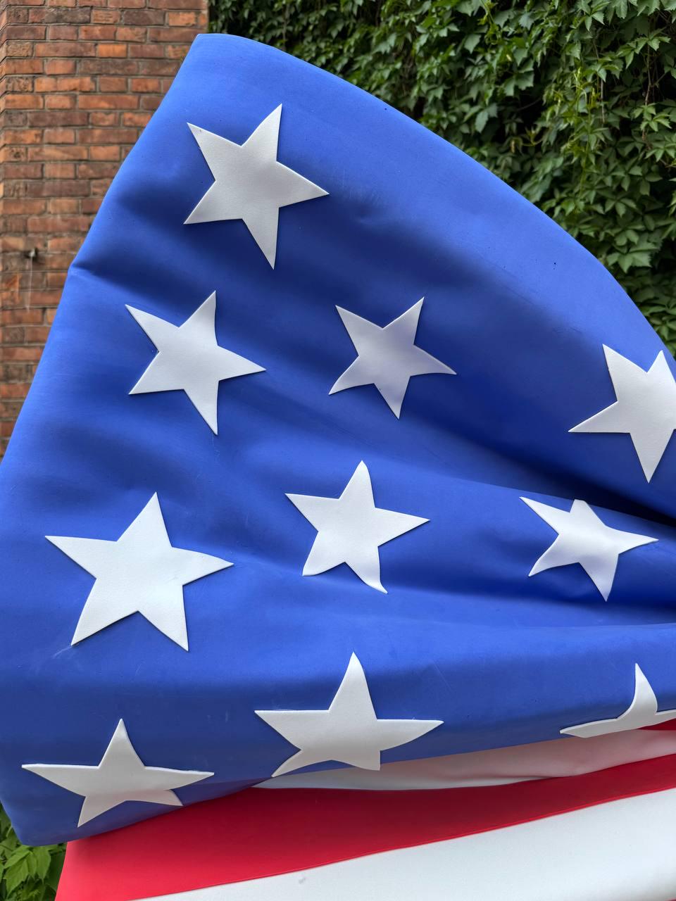May include: A close-up of the American flag, featuring a blue field with white stars and red and white stripes. The flag is made of a fabric material and is partially folded.