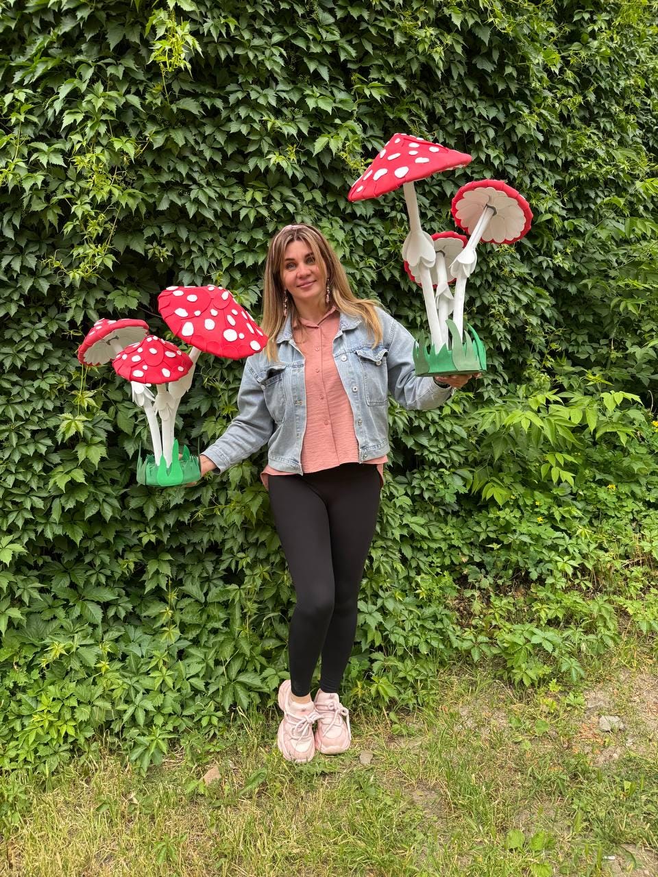 May include: Two decorative mushroom sculptures featuring bright red caps with white spots, white stems, and green grass-like bases. Each sculpture consists of multiple mushrooms of varying heights, constructed with a smooth, matte finish.