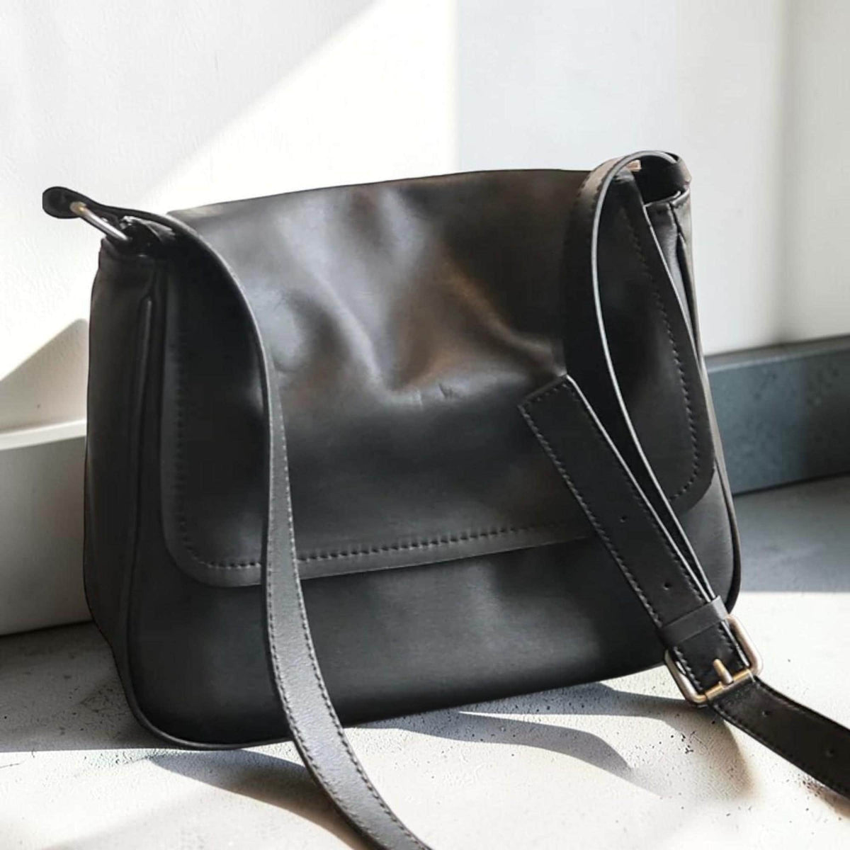 May include: A black leather messenger bag with a flap closure and adjustable shoulder strap. The bag features a rectangular shape with a stitched design and a metal buckle on the strap.