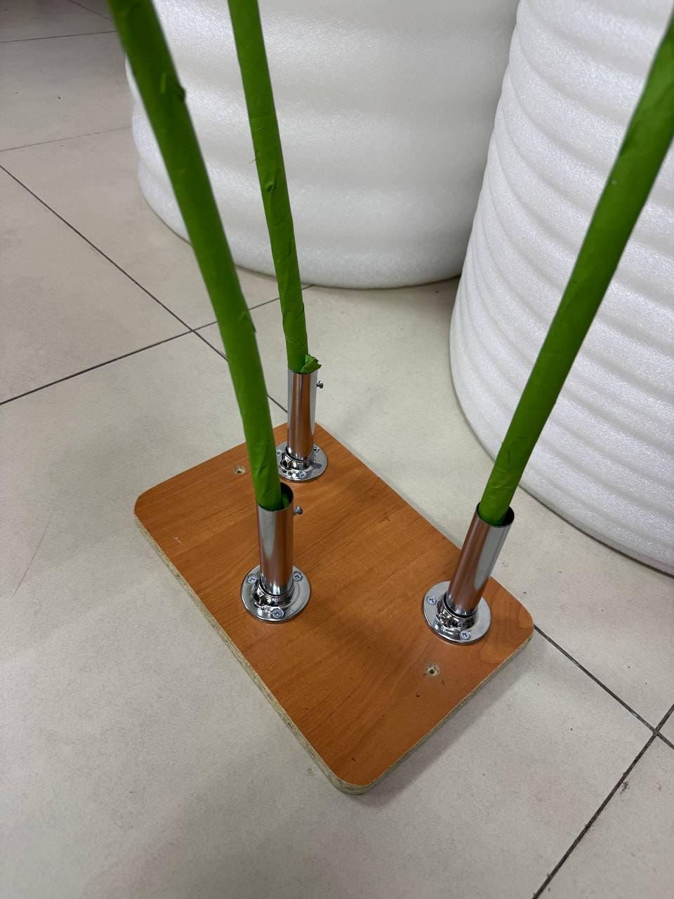 May include: A rectangular wooden base with a light brown finish featuring three chrome metal cylindrical mounts. Three bright green stems are inserted into the metal mounts, extending upward from the base in a vertical orientation.