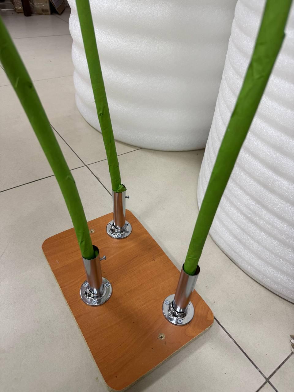 May include: A rectangular wooden base with a light brown finish featuring three chrome metal cylindrical mounts. Three long, thin, green-wrapped rods are inserted into the mounts, standing upright from the base in a vertical orientation.