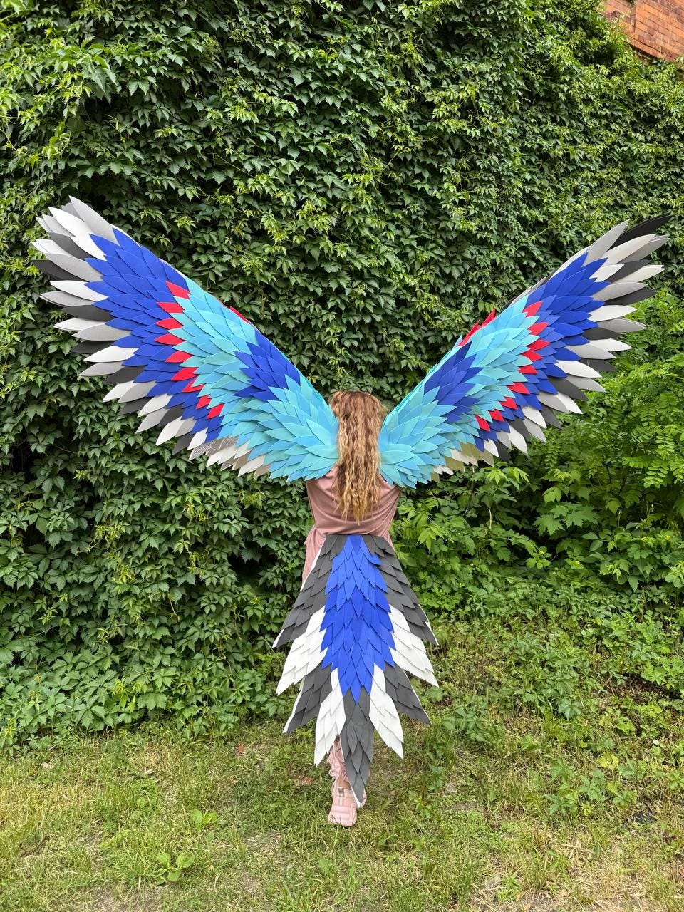 May include: Large bird-like wings and a matching tail piece featuring layered feathers in shades of royal blue, light blue, white, dark gray, and accents of red. The wingspan is wide and pointed, while the tail feathers are arranged in a fan.