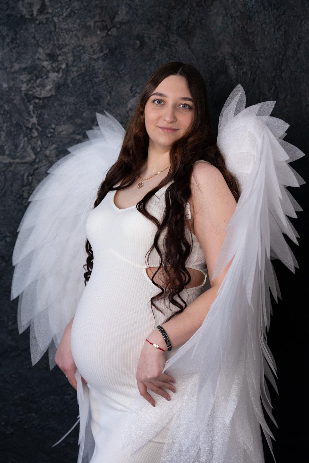 May include: A white ribbed sleeveless dress with side cutouts worn with large, layered white feathered wings. The dress features a scoop neckline and a form-fitting silhouette. The wings are constructed from multiple translucent, pointed white segments.