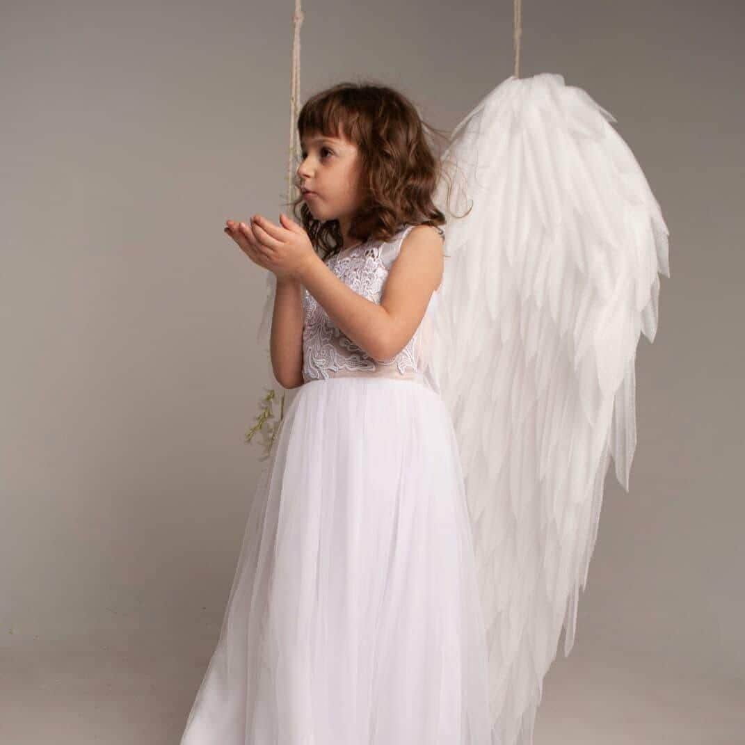 May include: A white sleeveless dress featuring a lace bodice with intricate floral embroidery and a long, flowing tulle skirt. Large, white, feathered-style angel wings are attached to the back, extending from the shoulders to the floor.