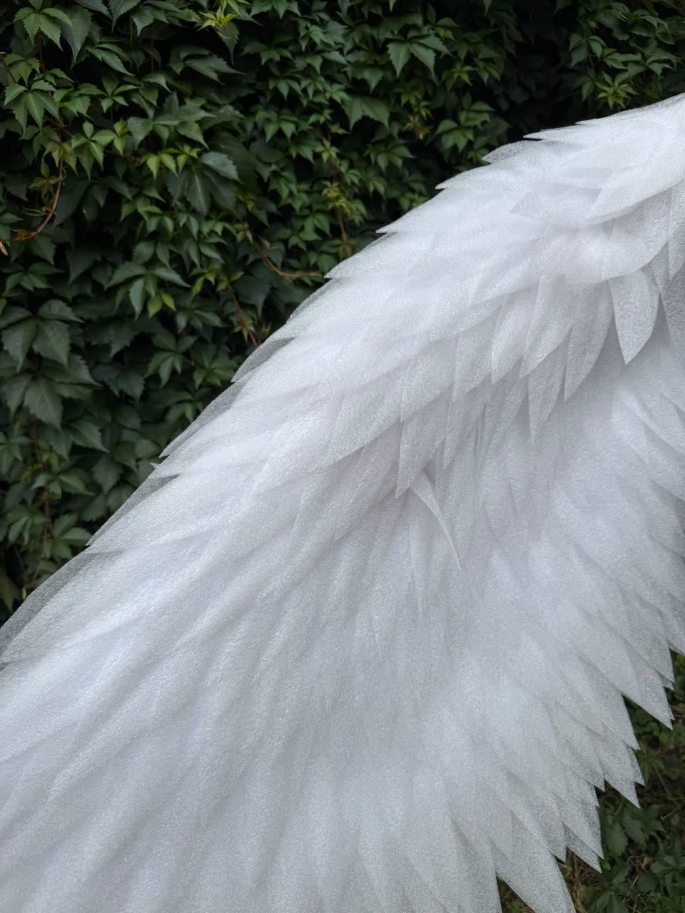 May include: A pair of large, white, layered wings constructed from individual, pointed, semi-translucent foam-like feather shapes. The structure features a dense, overlapping pattern that creates a textured, wing-like appearance with a subtle shimmer.