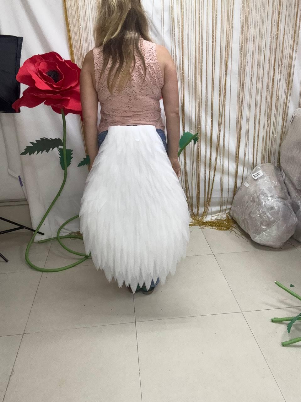 May include: A white, layered, feather-like tail accessory attached to the waist. The piece features multiple overlapping, pointed, white fabric segments that create a textured, plumage-inspired appearance, extending from the lower back downwards.
