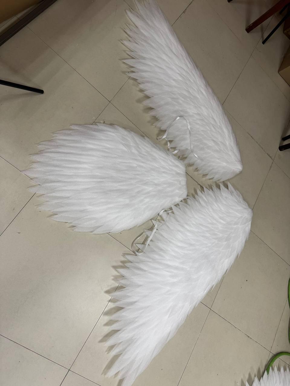 May include: Three white feathered wings arranged in a cluster. Each wing features layered, pointed white feathers with a soft texture. The wings include thin white ribbon straps attached to the base for securing the pieces to a garment or frame.