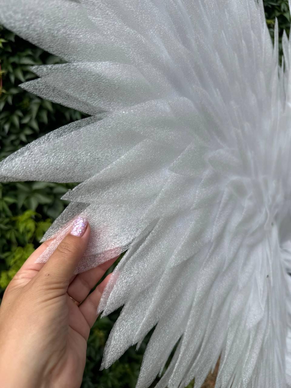 May include: A pair of large, white, wing-shaped decorations constructed from layered, semi-translucent, foam-like material. The individual segments are pointed and arranged in a fan-like pattern to resemble feathers, creating a textured surface.