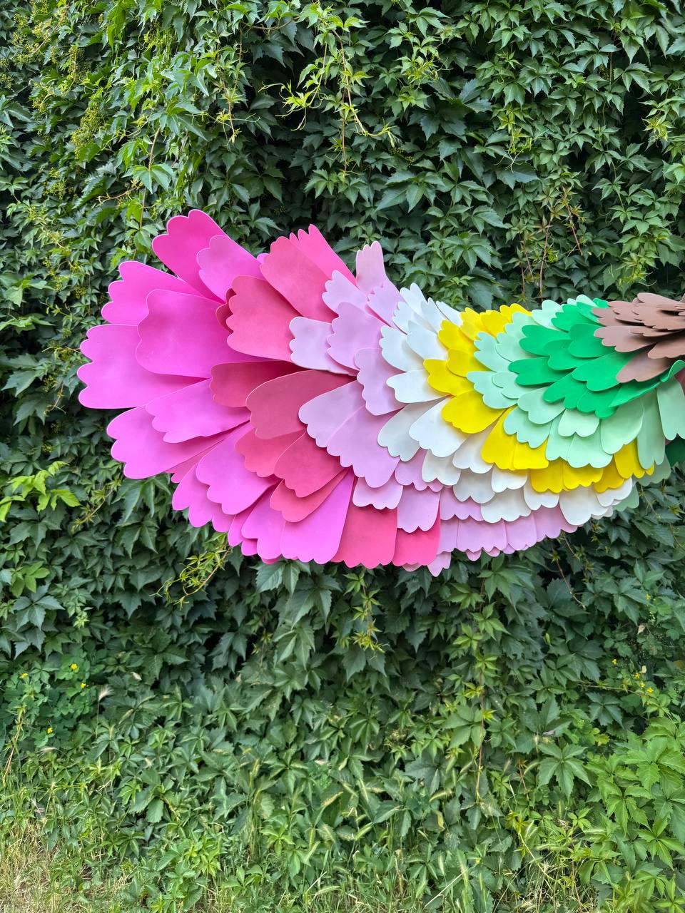 May include: A decorative fan-shaped accessory constructed from layered, scalloped-edge foam pieces in a vibrant gradient of colors, transitioning from deep magenta and pink to light pink, white, yellow, light green, dark green, and brown.