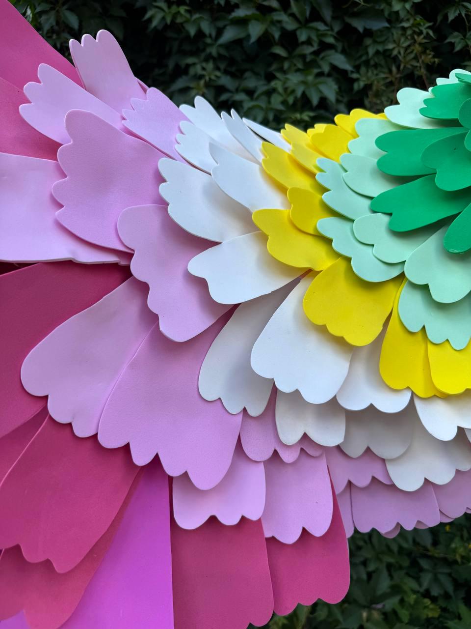 May include: A decorative wing structure composed of layered, scalloped-edge foam pieces in a vibrant rainbow gradient. The colors transition from deep magenta and light pink to white, bright yellow, pale mint green, and solid forest green.