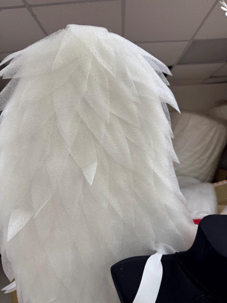 May include: A pair of white angel wings constructed from layered, diamond-shaped foam sheets. The wings feature a textured, semi-translucent surface with pointed edges arranged in a cascading pattern, attached to a black base with white elastic straps.