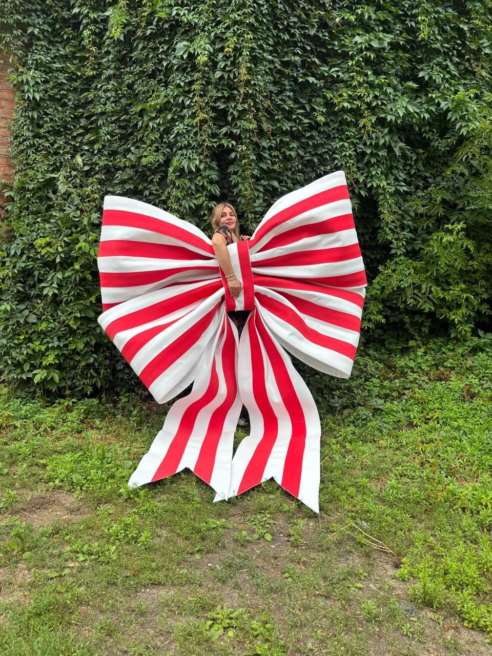 May include: An oversized decorative bow featuring bold, vertical red and white stripes. The large, structured accessory has two wide loops and two long, trailing ribbon ends that extend downward, creating a prominent, eye-catching display piece.