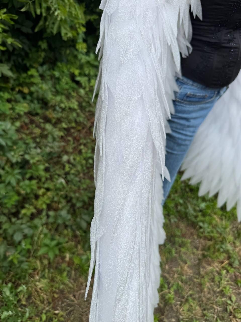 May include: A pair of large, white, glittery, feathered wings constructed with layered, pointed, foam-like material. The wings feature a textured, shimmering surface that catches the light, creating a distinct, layered appearance across the entire structure.