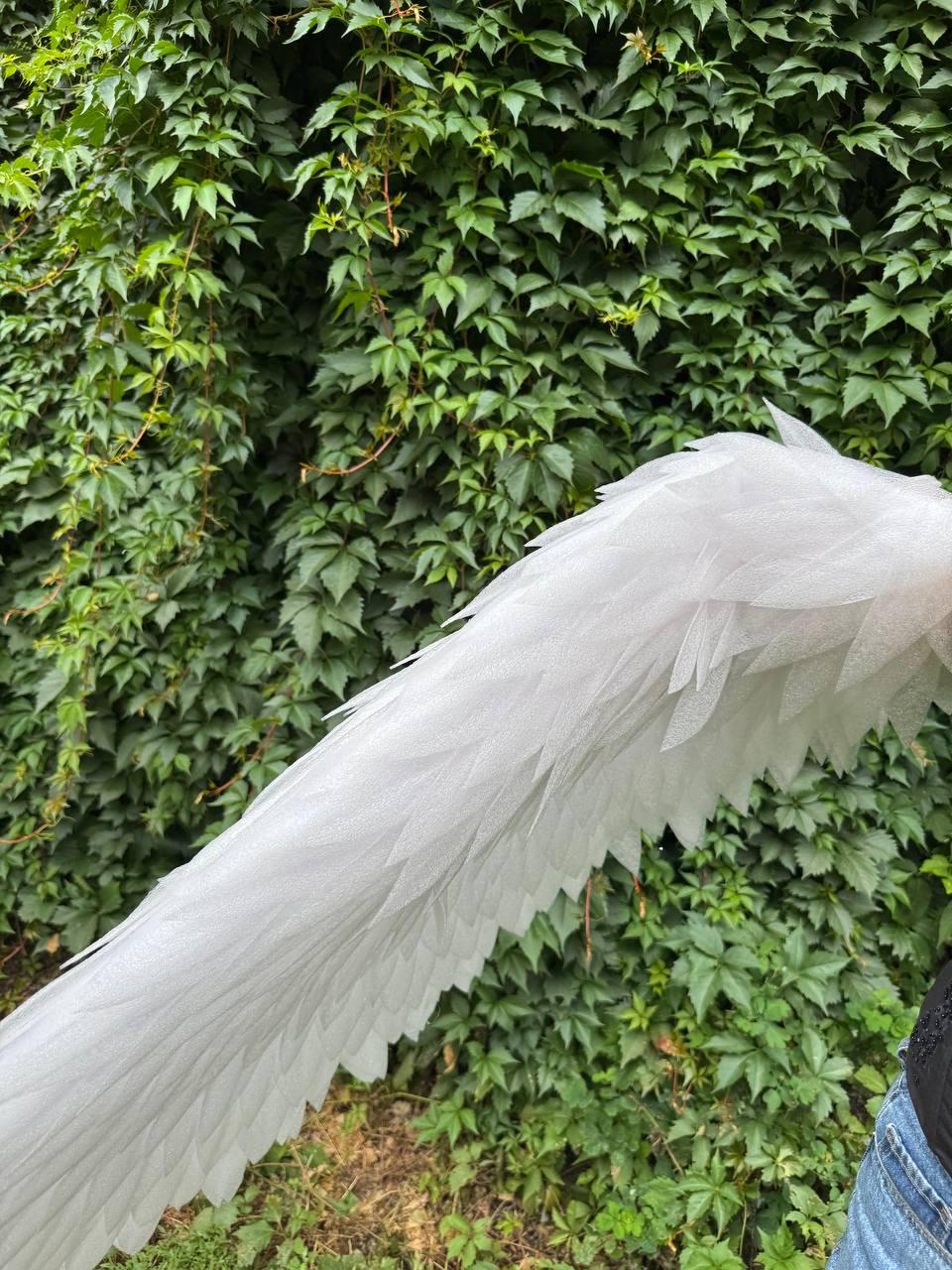 May include: A pair of large, white, feathered-style wings constructed from layered, semi-translucent, pointed fabric pieces. The wings feature a textured, shimmering surface and are arranged in a cascading, overlapping pattern to mimic natural plumage.
