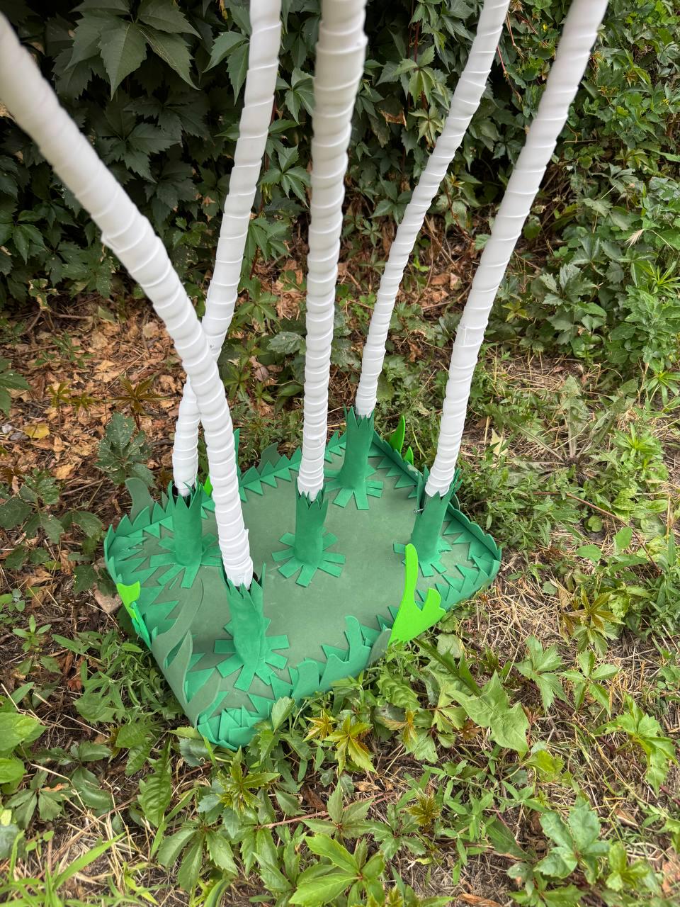 May include: A rectangular green base with jagged, grass-like edges features five tall, white, spiraled stems extending upward. The stems are attached to the base with green, star-shaped supports, creating a structure that resembles a stylized plant.