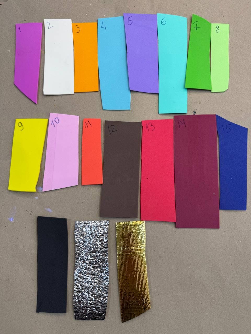May include: A collection of fifteen rectangular foam strips arranged in three rows, each labeled with a handwritten number from 1 to 15. The strips feature a variety of solid colors including purple, white, orange, blue, green, yellow, pink, red, brown, black, silver, and gold.