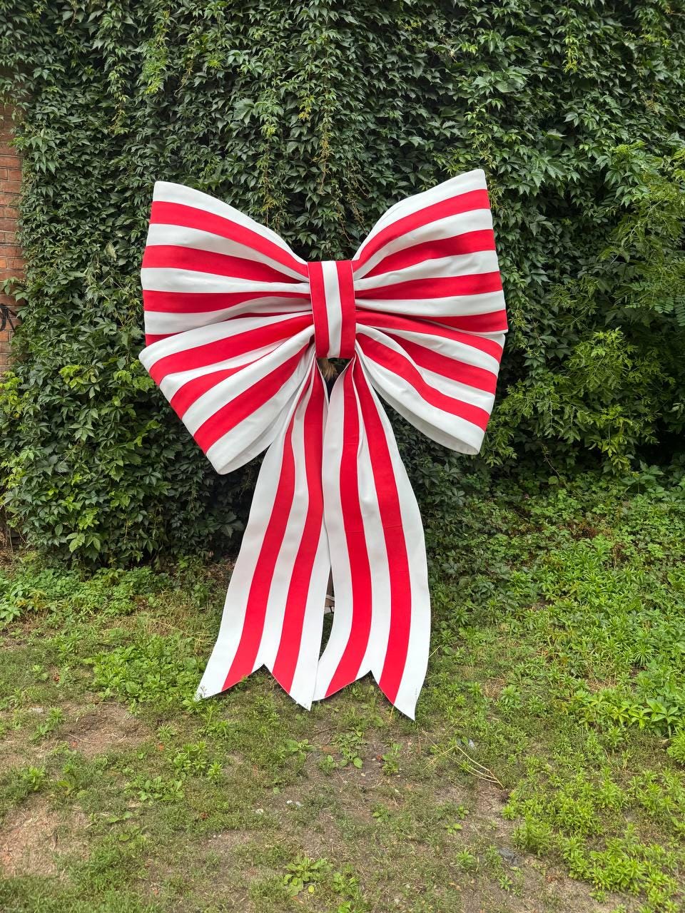 May include: A large decorative bow featuring a repeating pattern of vertical red and white stripes. The bow has two wide, voluminous loops at the top and two long, flowing tails hanging downward, each ending in a V-shaped notch at the bottom edge.
