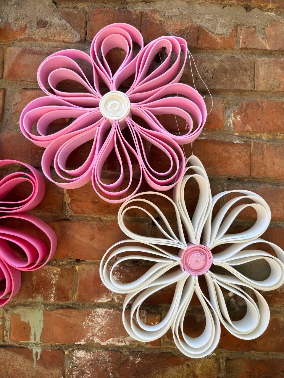 May include: Two decorative wall flowers constructed from looped strips of material. The top flower is solid pink with a white center, while the bottom flower is solid white with a pink center. Each flower features eight symmetrical, rounded petals.