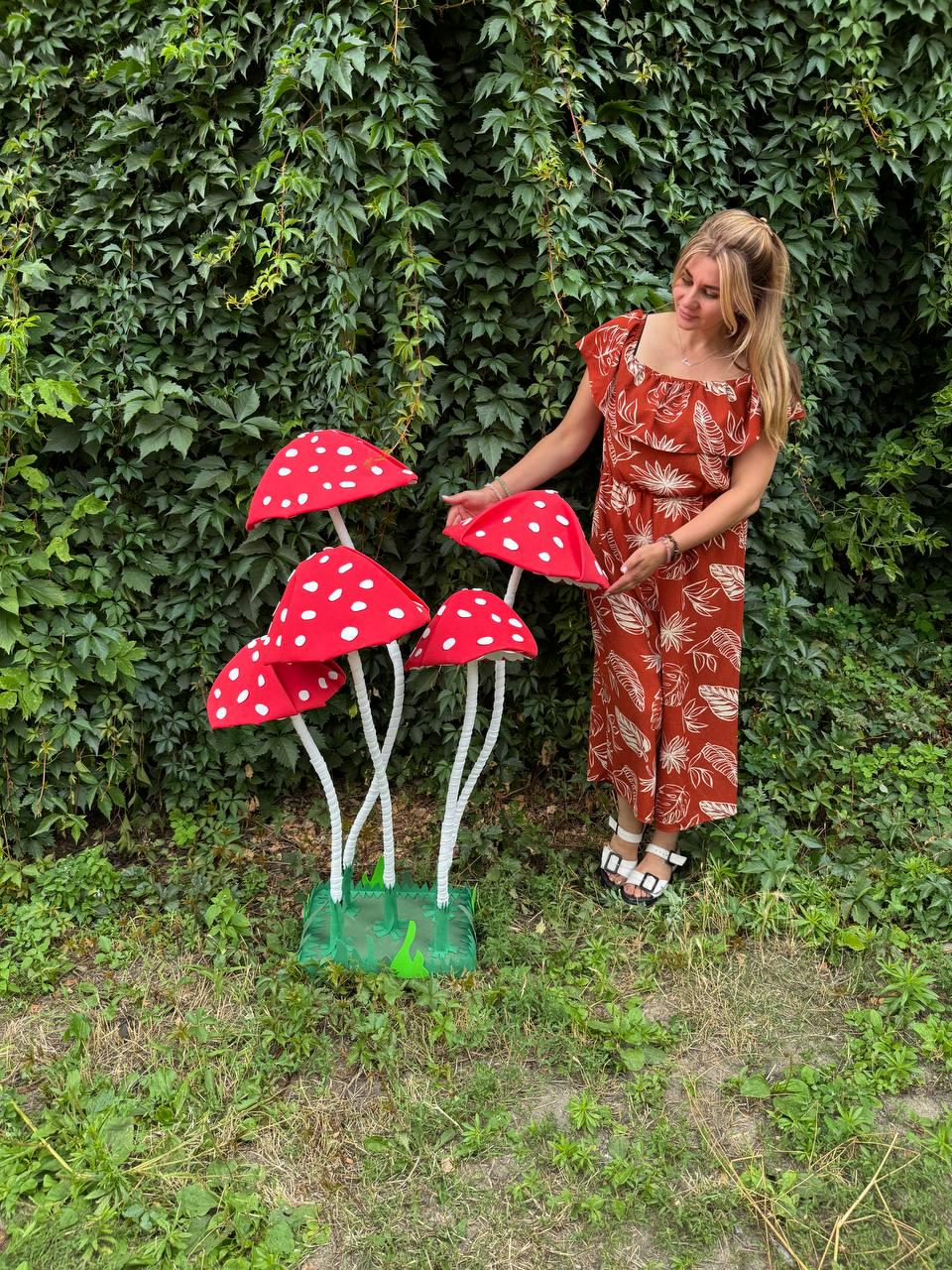 May include: A decorative floor sculpture featuring four large, red mushroom caps with white polka dots, supported by slender white stems rising from a green square base with jagged edges, designed as a whimsical garden or indoor display piece.