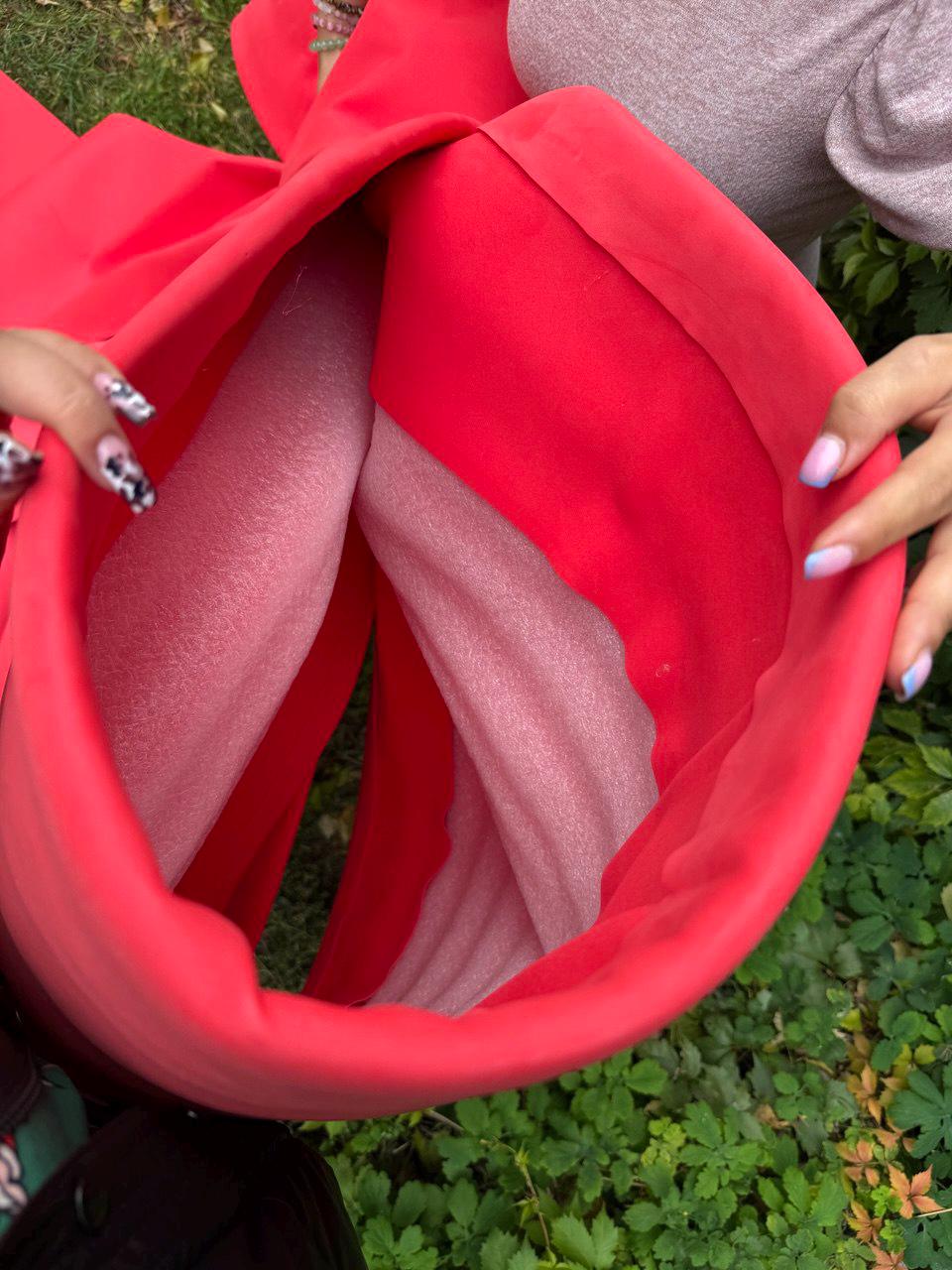 May include: A bright red, cylindrical container or sleeve featuring a smooth, matte exterior surface. The interior is lined with a pale pink, textured foam material that provides structure and padding to the flexible, vibrant red outer shell.