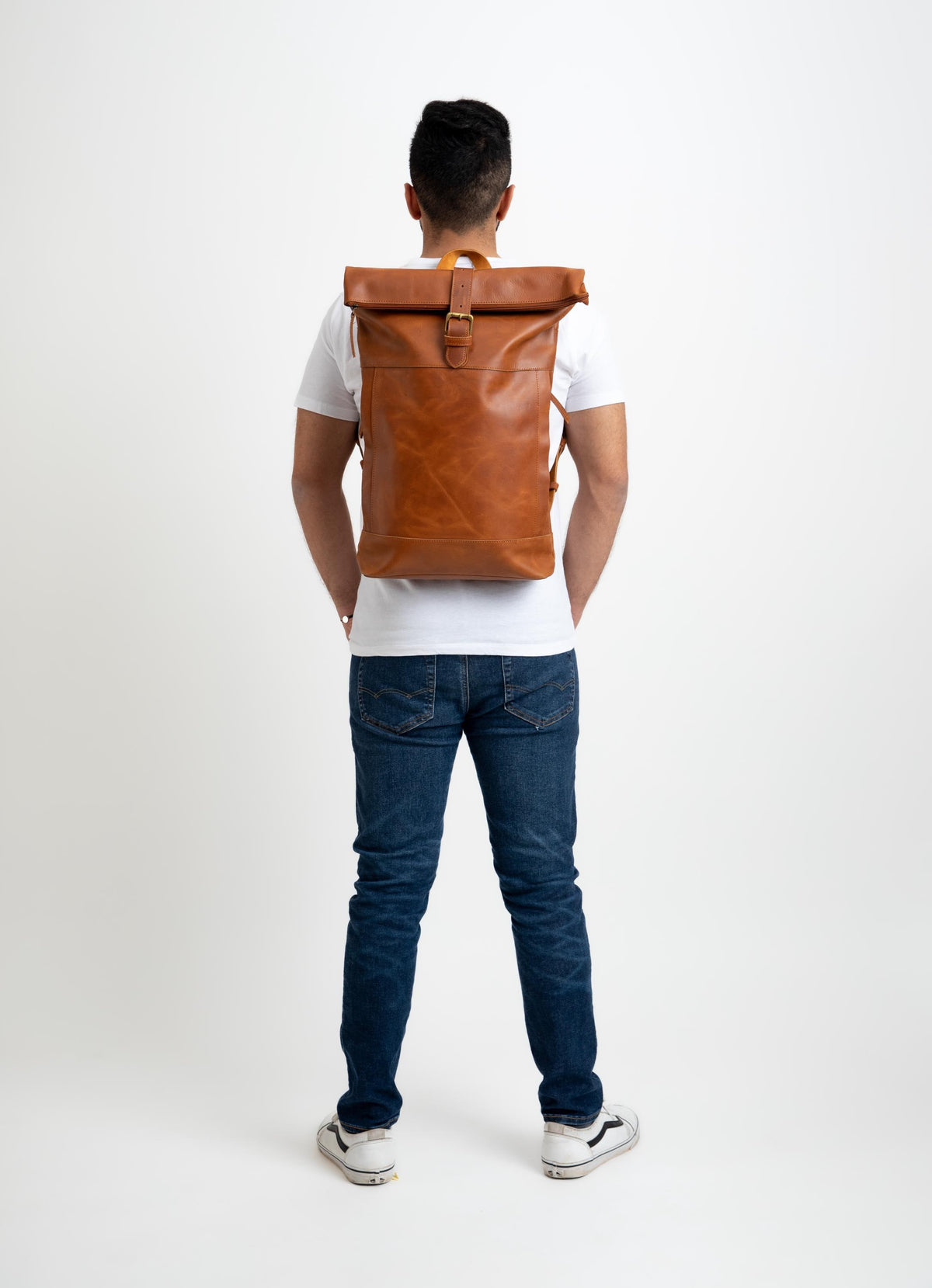 May include: A tan leather roll-top backpack featuring a single vertical strap with a metal buckle closure at the center. The bag has a smooth, matte finish and is worn on the back, showcasing a rectangular shape with a folded top section.
