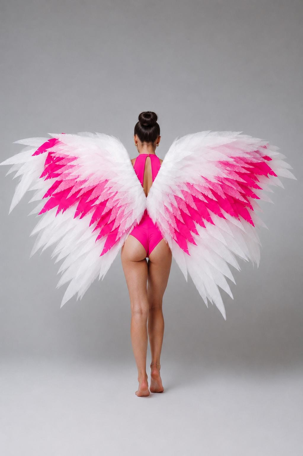 May include: Large decorative wings featuring a layered feather design with a gradient color scheme transitioning from white at the tips to vibrant hot pink in the center. The wings are worn over a solid hot pink bodysuit with a high neckline.