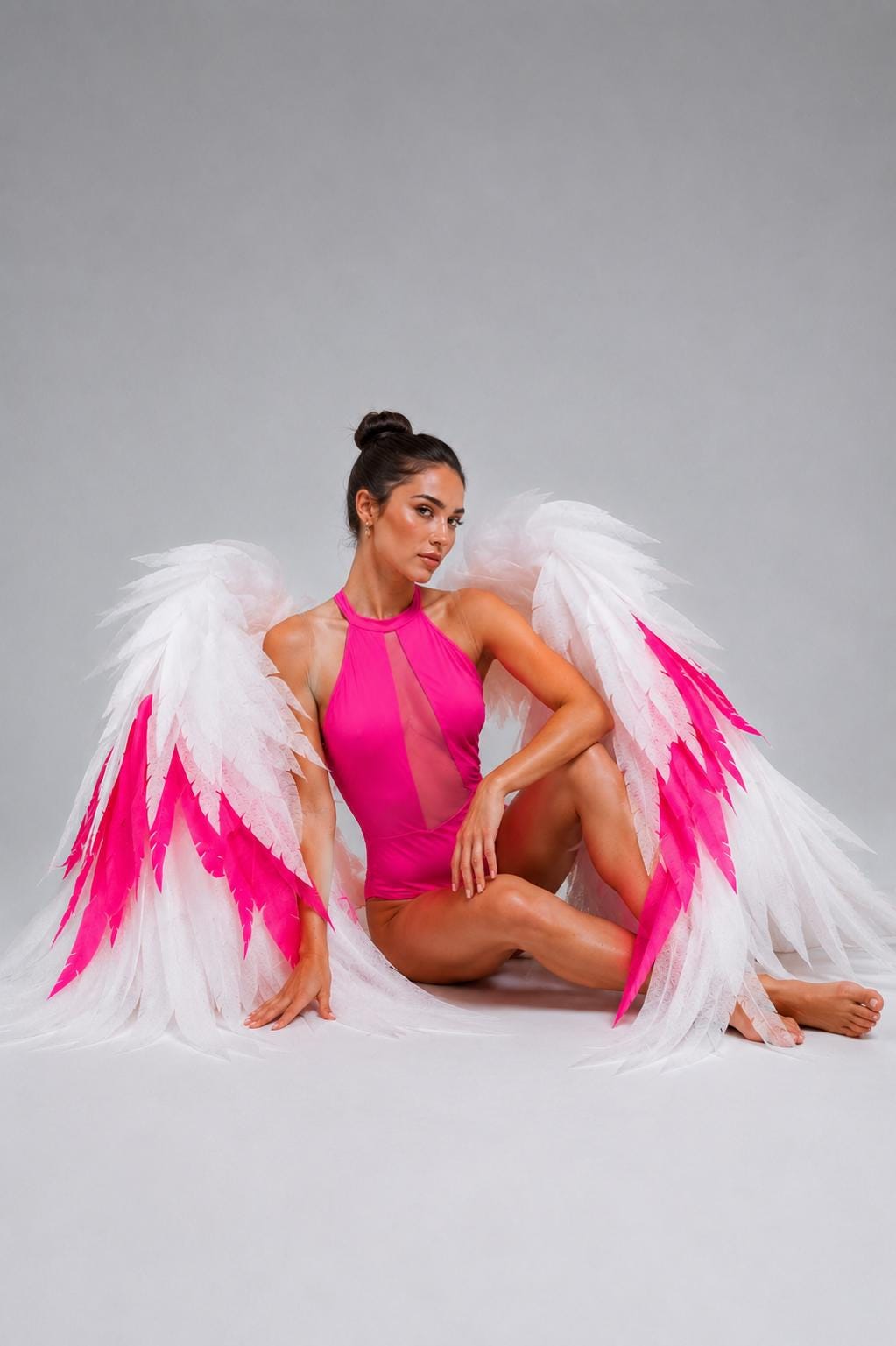 May include: A bright pink bodysuit featuring a high halter neckline with a vertical sheer mesh panel down the center, paired with large, expansive decorative wings composed of layered white feathers with vibrant hot pink accents at the tips.