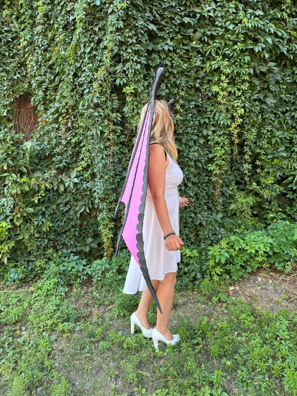 May include: A pair of tall, pointed dragon wings featuring a vibrant pink center panel with a black scalloped border and a black frame. The wings are worn over a simple white sleeveless dress paired with white high-heeled shoes.